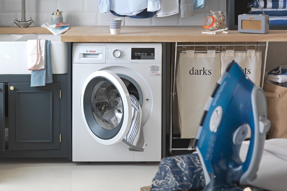 A white washing machine in a utility room under a wooden counter.